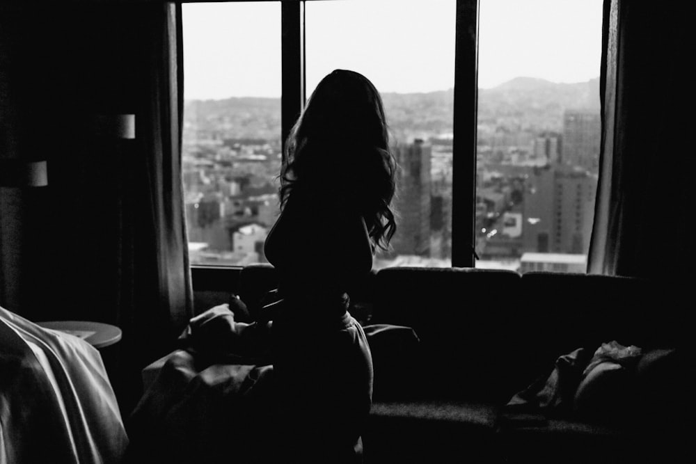 a black and white photo of a woman looking out a window