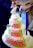 A multi-tiered cake covered with pink rose-shaped decorations and green leaves. The cake has a neat arrangement of small, round embellishments and is topped with a bride and groom figurine holding a bouquet of flowers. The design is intricate and elegant, suitable for a wedding.