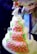 A multi-tiered cake covered with pink rose-shaped decorations and green leaves. The cake has a neat arrangement of small, round embellishments and is topped with a bride and groom figurine holding a bouquet of flowers. The design is intricate and elegant, suitable for a wedding.