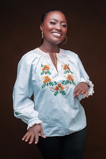 A joyful woman wearing multiple delicate accessories, smiling softly against a white background.