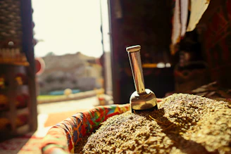 A warm kitchen scene showing a woman gently grinding spices on a sil batta with natural sunlight streaming in.