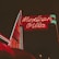 A brightly illuminated neon sign in red and green advertises 'Mexican Villa' against a dark night sky. The sign features stylized text with a retro aesthetic and is attached to a building that appears slightly in the background.