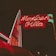 A brightly illuminated neon sign in red and green advertises 'Mexican Villa' against a dark night sky. The sign features stylized text with a retro aesthetic and is attached to a building that appears slightly in the background.