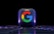 A three-dimensional glossy cube featuring the colorful Google logo against a dark background. The cube displays a reflective surface, capturing hints of surrounding lights, and is placed on a surface with subtle lighting effects.
