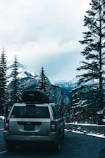 A comfortable SUV parked beside a mountain trail with a backdrop of snow-capped peaks.