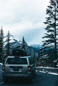 A spacious white SUV parked in front of a mountain lodge surrounded by tall pine trees.