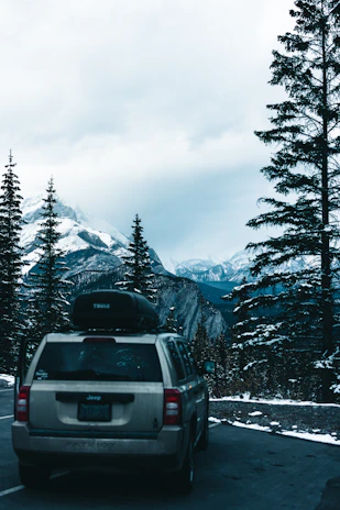 A comfortable SUV parked beside a mountain trail with a backdrop of snow-capped peaks.