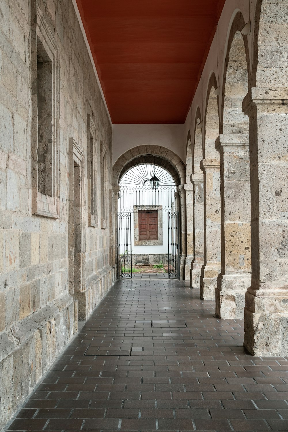 a brick walkway with arches and a clock on the wall
