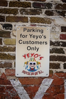 A sign mounted on a textured brick wall reads 'Parking for Yeyo's Customers Only' with a colorful logo beneath featuring a cartoon character wearing a sombrero and large googly eyes, representing Yeyo's Mexican Grill.