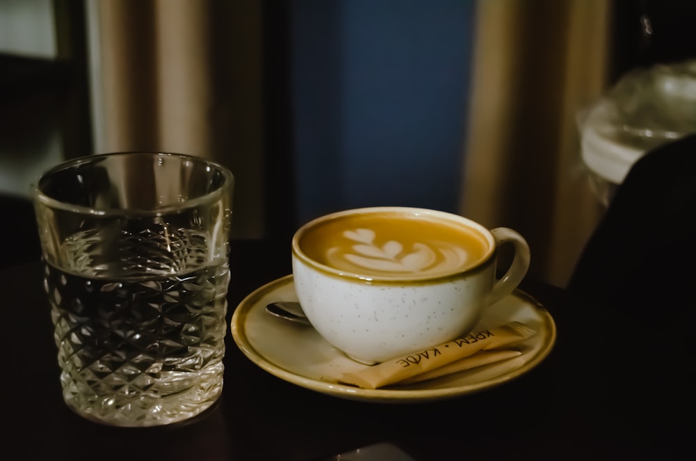 a cup of coffee on a saucer next to a glass of water