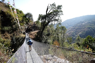 a man walking across a suspension bridge in the mountains
