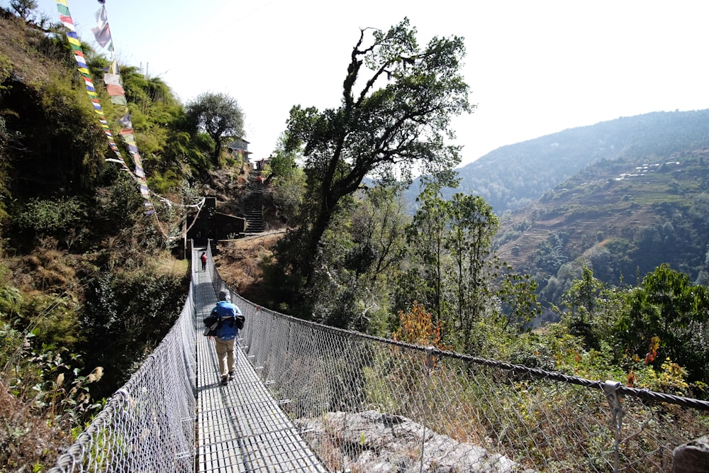 a man walking across a suspension bridge in the mountains