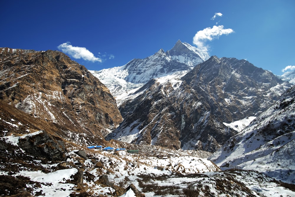 a snowy mountain range with a blue tent in the foreground