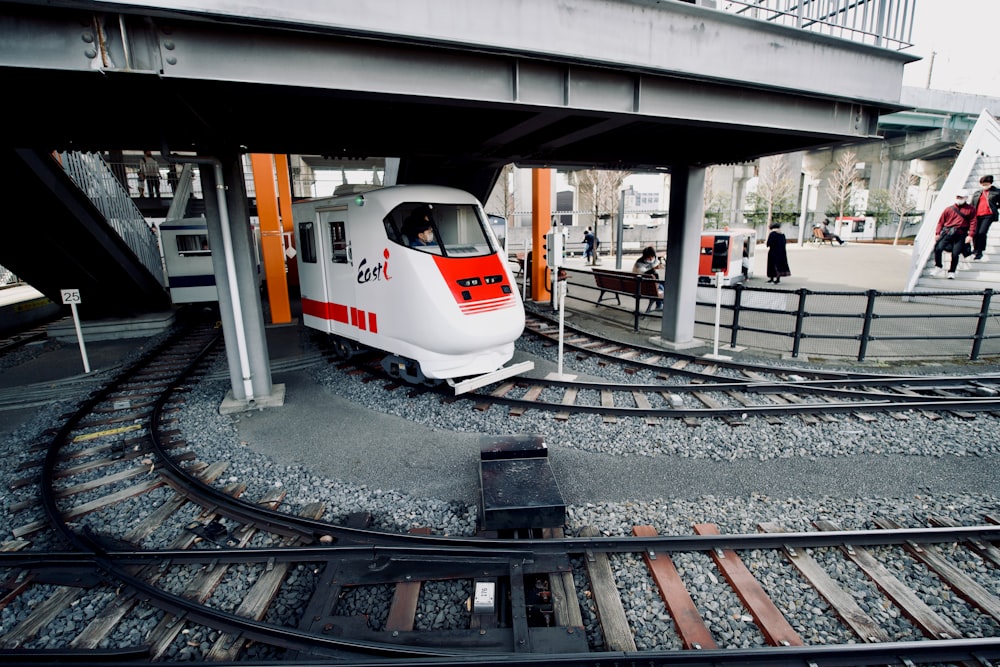 a white and red train traveling under a bridge