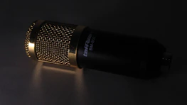 Close-up of a microphone with black and gold accents in a studio.