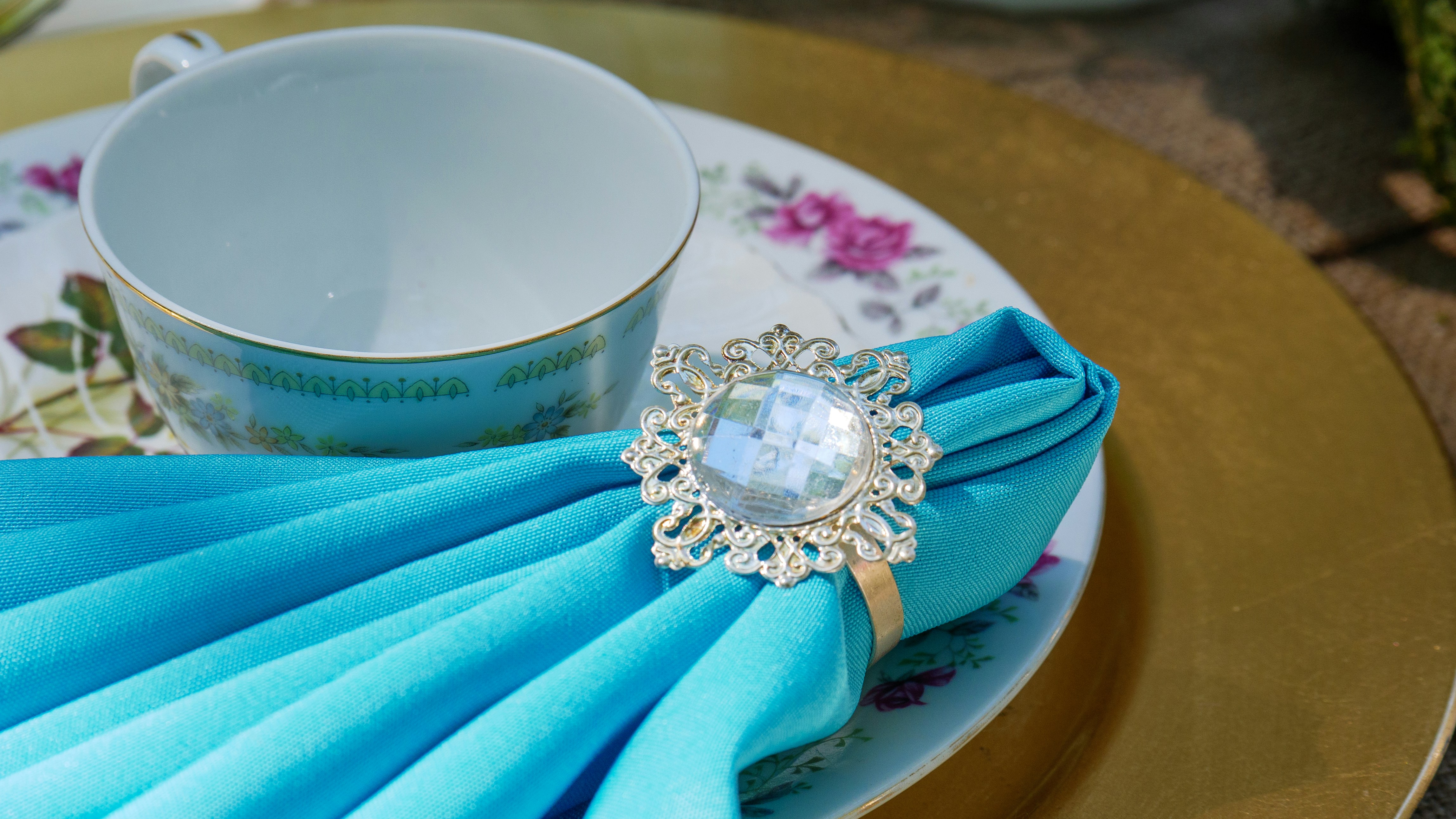 A floral teacup and napkin sit on a decorative table.