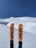 Two skis with the brand name '4FRNT' stand upright in the foreground against a backdrop of pristine, untouched snow and a clear blue sky.