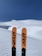 Two skis with the brand name '4FRNT' stand upright in the foreground against a backdrop of pristine, untouched snow and a clear blue sky.