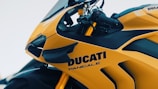A close-up shot of a bright yellow Ducati Panigale motorcycle, showcasing its sleek design and sport features. The brand and model name are prominently displayed on the side of the bike. The handlebar and part of the windscreen are visible, highlighting its aerodynamic structure.