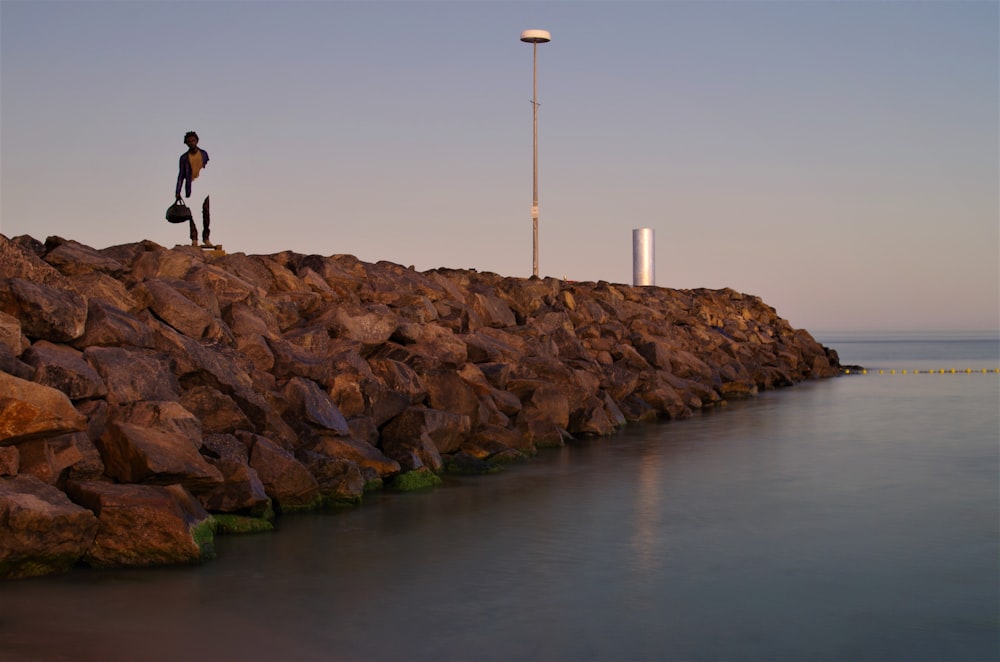 a man standing on a rock wall next to a body of water