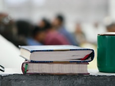 a stack of books sitting next to a green coffee mug