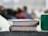 Two books with colorful bindings are stacked on a rough-textured surface, alongside a green cup. In the background, several blurred figures, suggesting a classroom or seminar setting, are visible, adding depth to the scene.