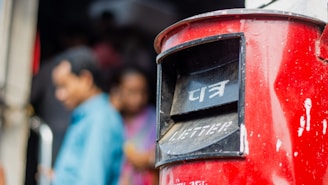 a close up of a red mailbox with people in the background