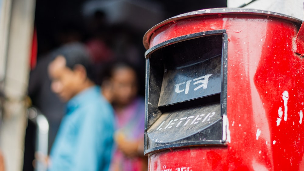 a close up of a red mailbox with people in the background