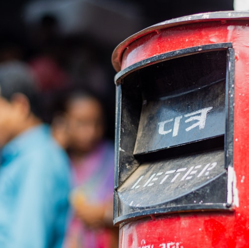 a close up of a red mailbox with people in the background