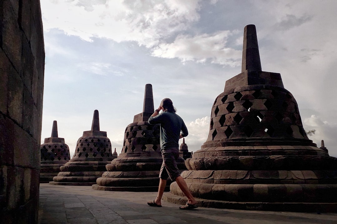 a man walking past a large stone structure, A walk through time at Borobudur Temple