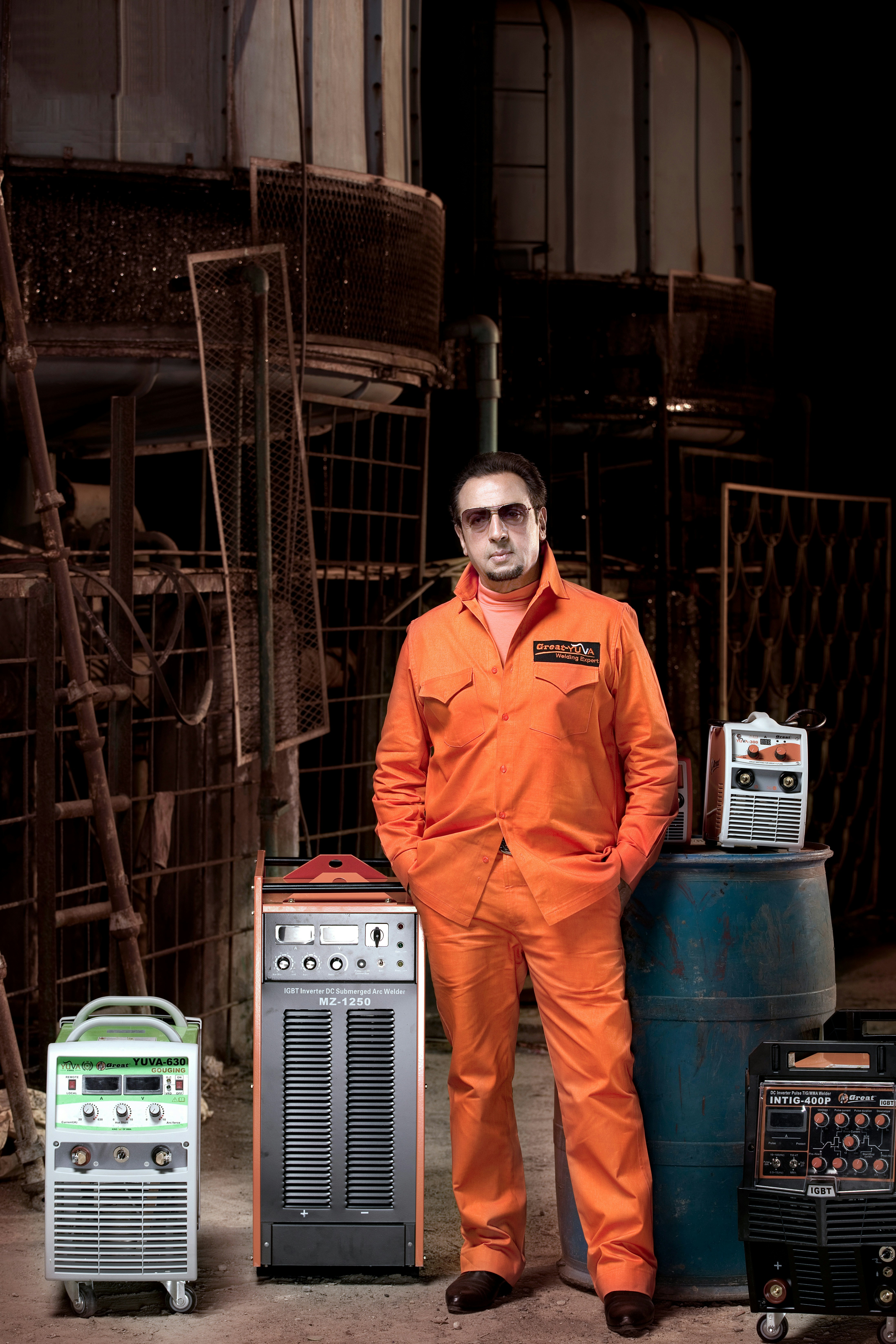 Welder in an orange uniform standing by industrial machines.