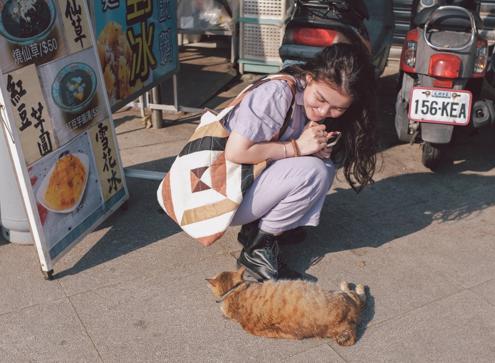 a woman kneeling down next to a cat