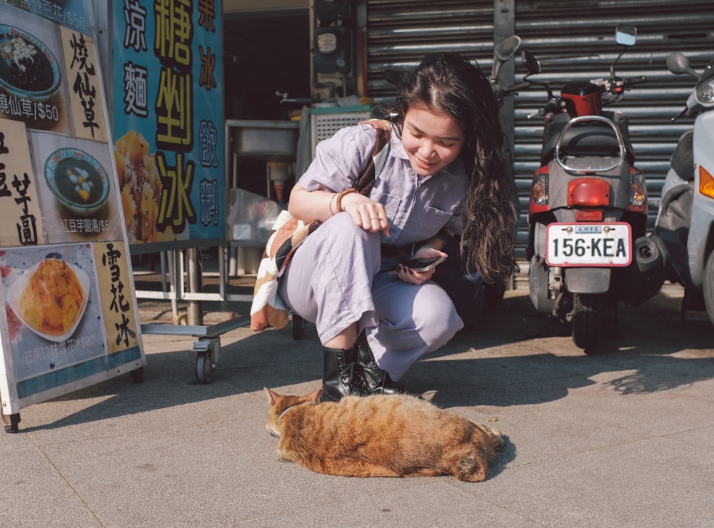 a woman kneeling down next to a cat