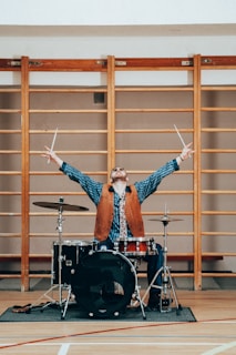 a man standing behind a drum set on top of a hard wood floor