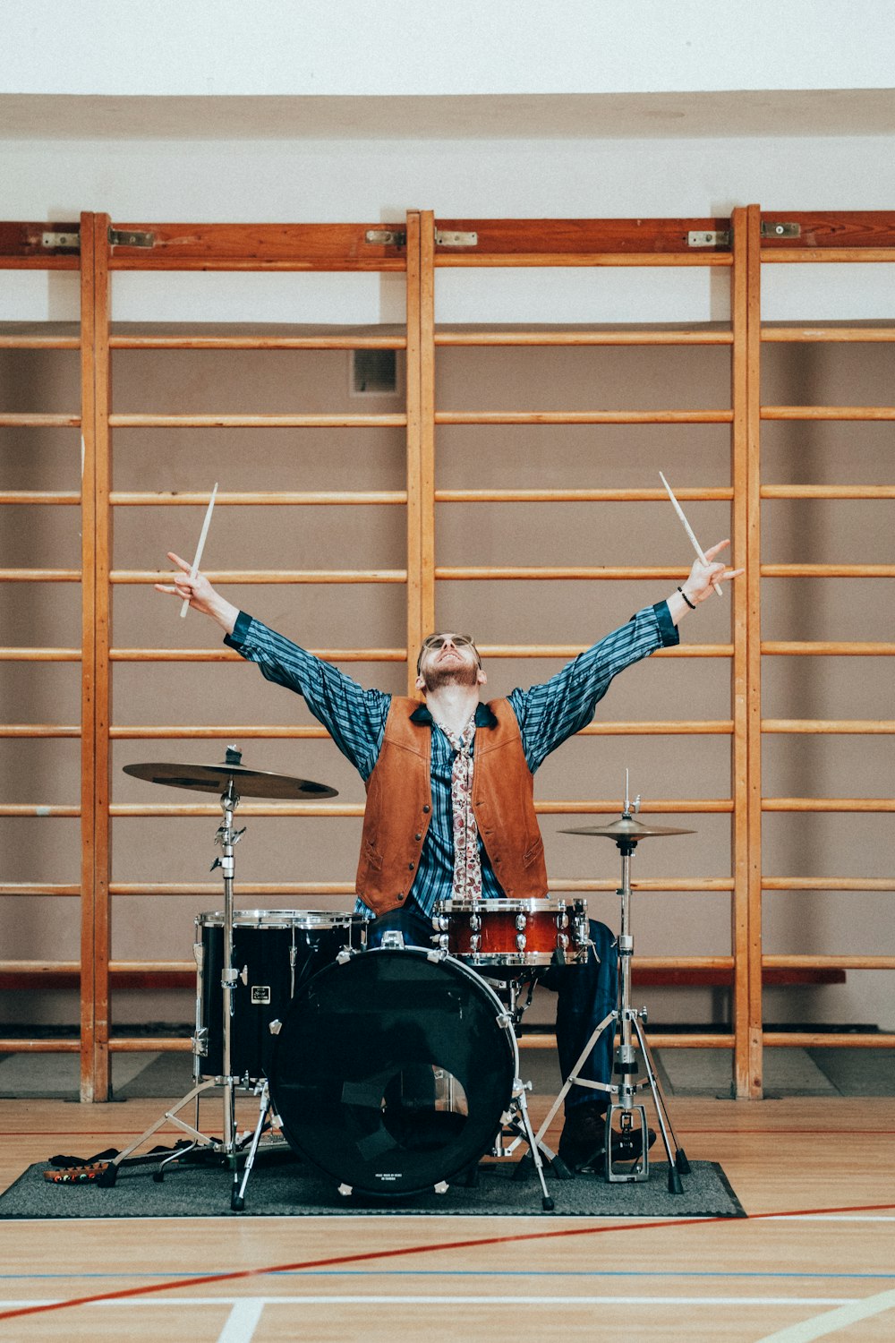 a man standing behind a drum set on top of a hard wood floor