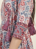 Detailed patterns featuring floral and geometric designs cover a portion of a dress. The fabric is adorned with red, blue, and white colors, and includes decorative tassels along the seam.