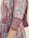 Detailed patterns featuring floral and geometric designs cover a portion of a dress. The fabric is adorned with red, blue, and white colors, and includes decorative tassels along the seam.