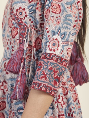 Detailed patterns featuring floral and geometric designs cover a portion of a dress. The fabric is adorned with red, blue, and white colors, and includes decorative tassels along the seam.
