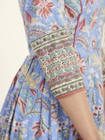 An intricately designed garment featuring floral and botanical patterns in vibrant colors. The fabric is primarily blue with red, green, and yellow accents. The sleeve has detailed embroidery with geometric and floral motifs.