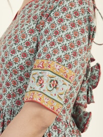 A fabric with a detailed floral pattern in red and orange against a light green background. The sleeve features an ornate design with yellow, red, and green floral and vine motifs, bordered by a red trim.