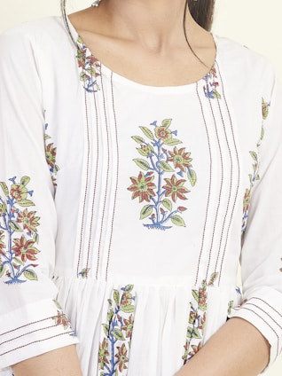 A close-up of a garment featuring intricate floral embroidery patterns with red, green, and blue colors on a white fabric. The design includes vertically aligned lines and floral motifs positioned symmetrically.