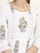 A close-up of a garment featuring intricate floral embroidery patterns with red, green, and blue colors on a white fabric. The design includes vertically aligned lines and floral motifs positioned symmetrically.