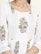 A close-up of a garment featuring intricate floral embroidery patterns with red, green, and blue colors on a white fabric. The design includes vertically aligned lines and floral motifs positioned symmetrically.