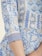 A close-up of a garment with intricate floral and geometric patterns in shades of blue and white. The fabric features lace detailing on the sleeve, creating an elegant and delicate appearance.