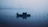 Fishing boat gliding over calm river waters at dawn with mist rising.