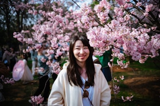 A smiling Brazilian woman enjoying a peaceful moment in a Japanese park during cherry blossom season.