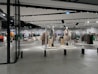 A modern clothing store with mannequins displaying beige and green outfits. The spacious, well-lit interior features neatly arranged racks of clothes and showcases a minimalist design. Spotlights hang from the ceiling, illuminating the display areas.