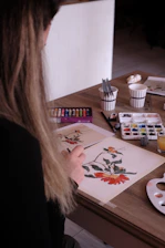 a woman sitting at a table working on a painting