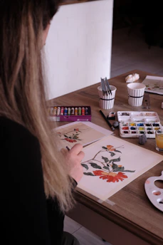 a woman sitting at a table working on a painting
