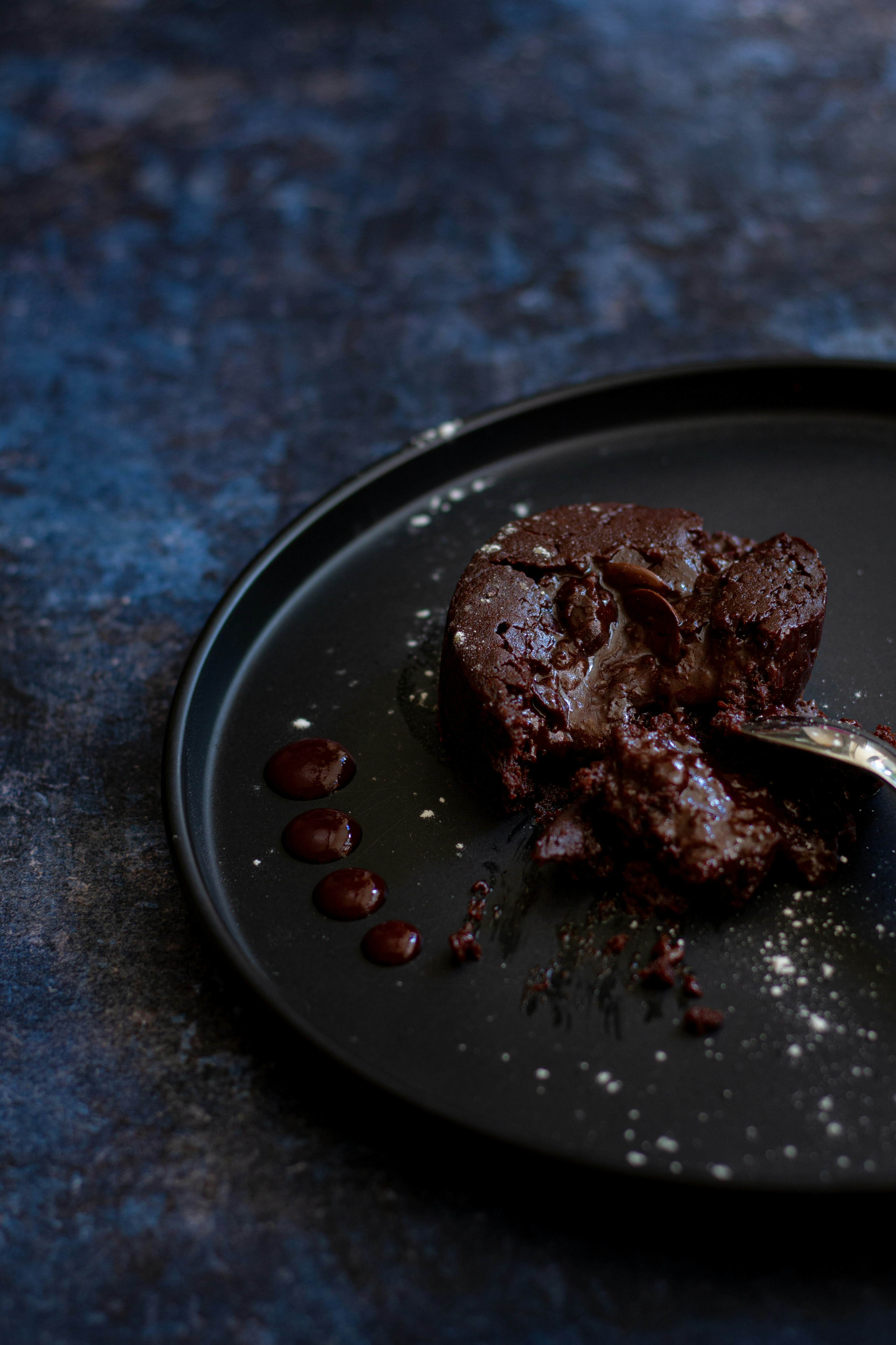 Warm dark chocolate fondant with molten centre flowing onto a white plate, dusted with cocoa